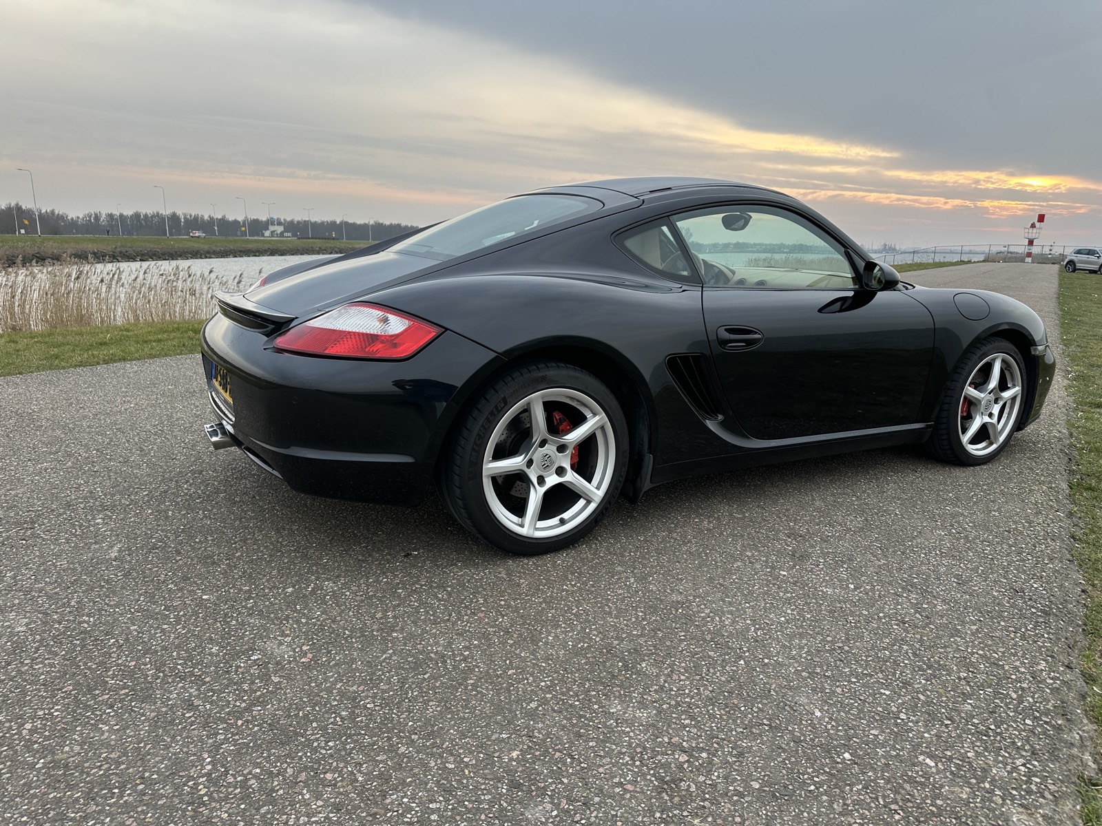 Zwarte Porsche Cayman bij zonsondergang op een dijk